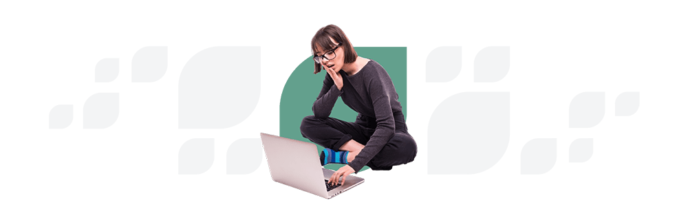 Young woman with glasses sitting on a transparent block, using a laptop, dressed in a black top and jeans, looking thoughtfully at the screen.