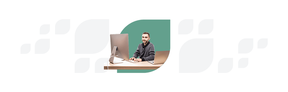 Man in a striped sweater sits at a desk with a computer and notebook, looking at the camera against a split white and teal background.
