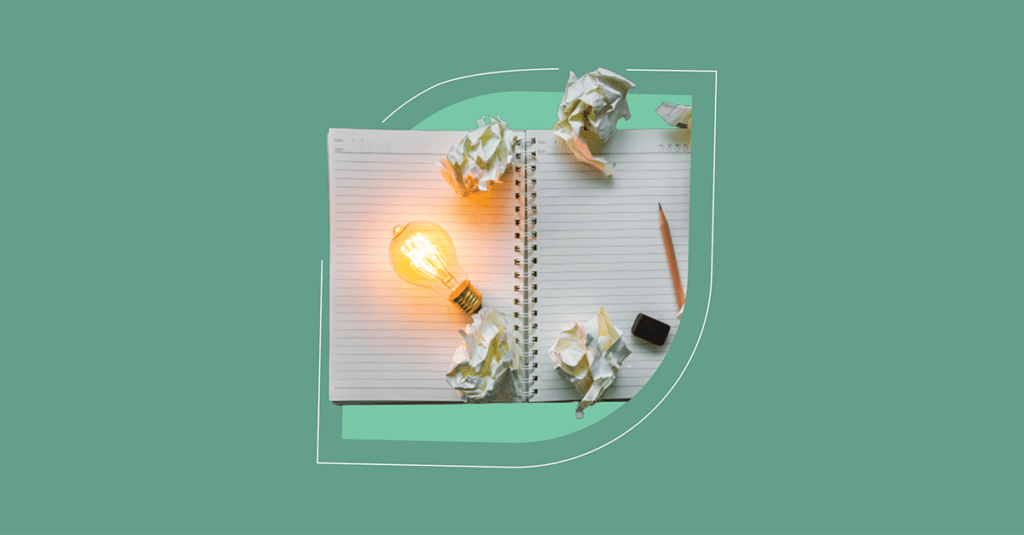 A glowing light bulb on an open notebook surrounded by crumpled paper balls, with a pencil and eraser, illustrates ITSM in 2023, symbolizing creativity and idea development in information technology