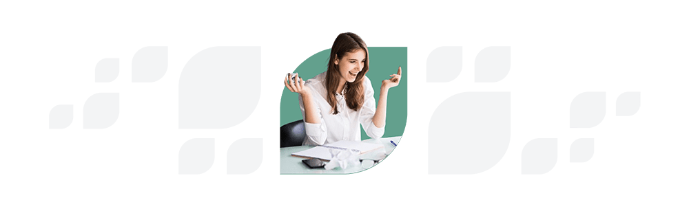A woman with brown hair gesturing excitedly at a laptop screen while sitting at a desk with papers.